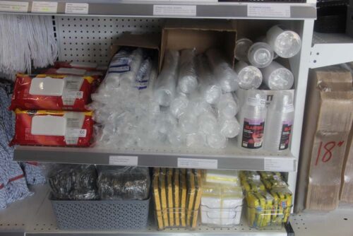 cleaning sponges, plastic silverware and plastic cups arranged on a shelf at C&C Suppliers